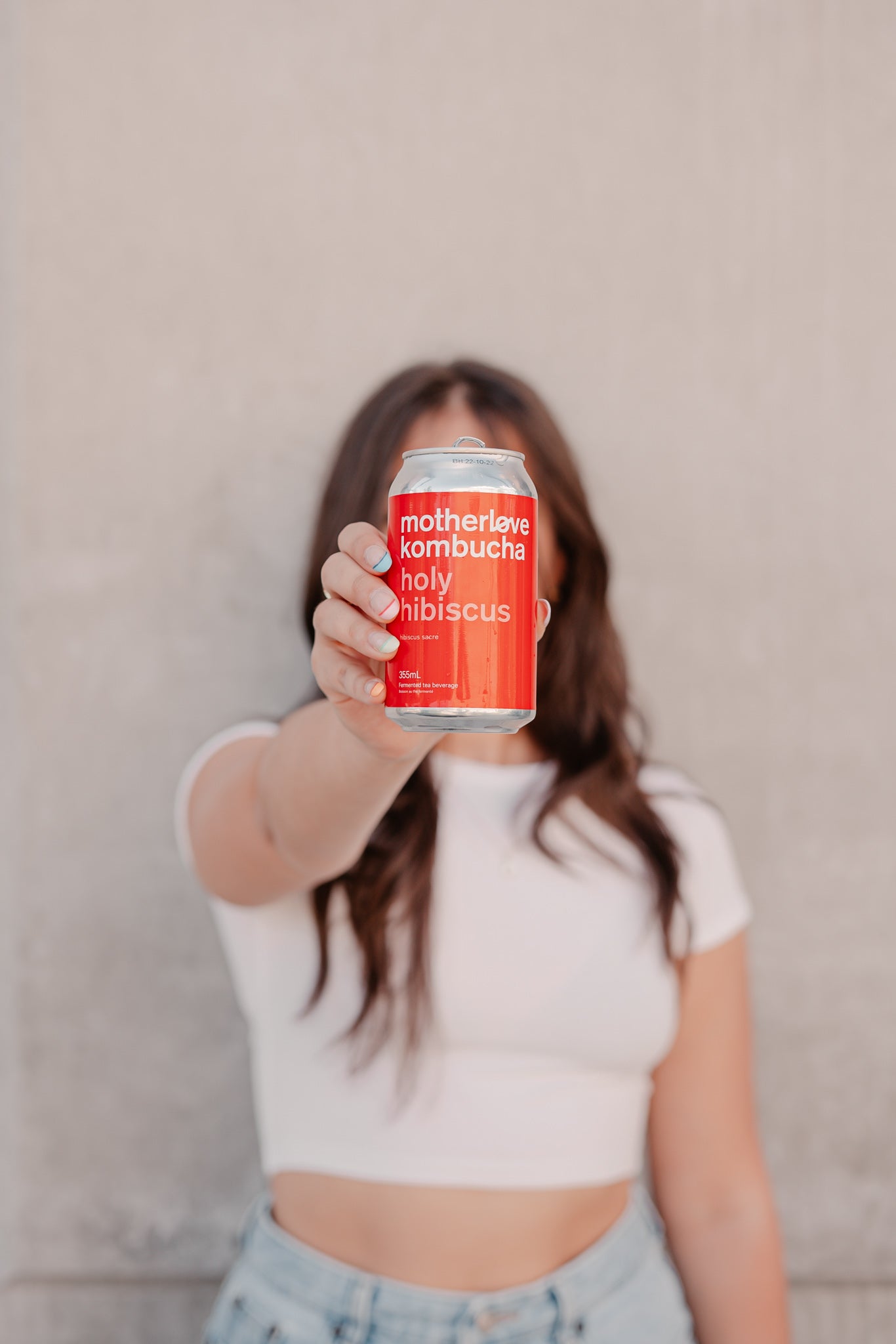 A woman holding a can of motherlove ferments Holy Hibiscus in front of her face